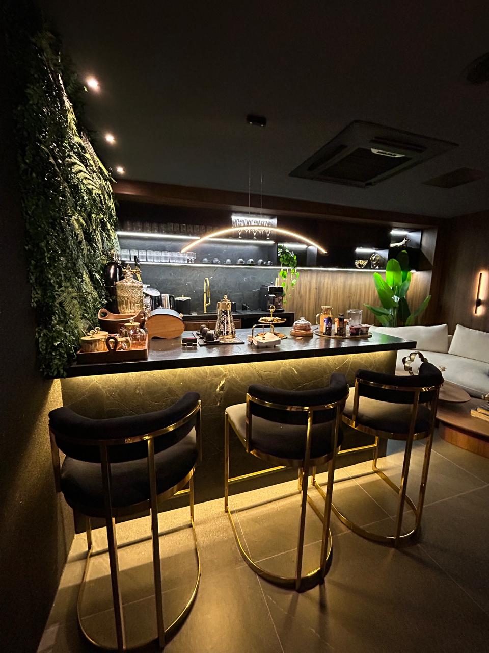 Bar do Bio Lounge Club com banquetas douradas, jardim vertical e balcão de pedra iluminado